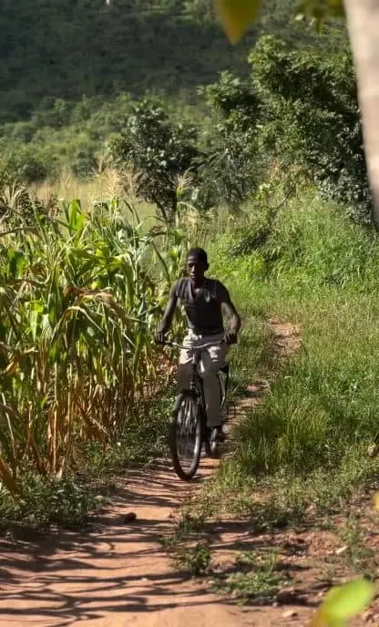 Daniel is pictured riding his bike down a small dirt path snaking between thick green grass.